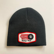 Laden Sie das Bild in den Galerie-Viewer, Black knit beanie style cap with embroidered Record Town patch on the front.
