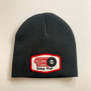 Black knit beanie style cap with embroidered Record Town patch on the front.